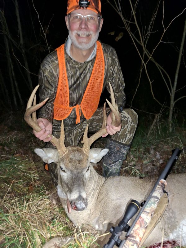 Hunter in orange safety gear with a harvested whitetail buck at night.