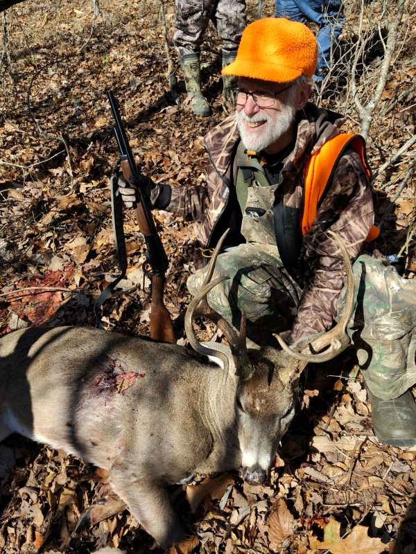 Hunter in orange safety gear with a harvested whitetail buck in the autumn woods.